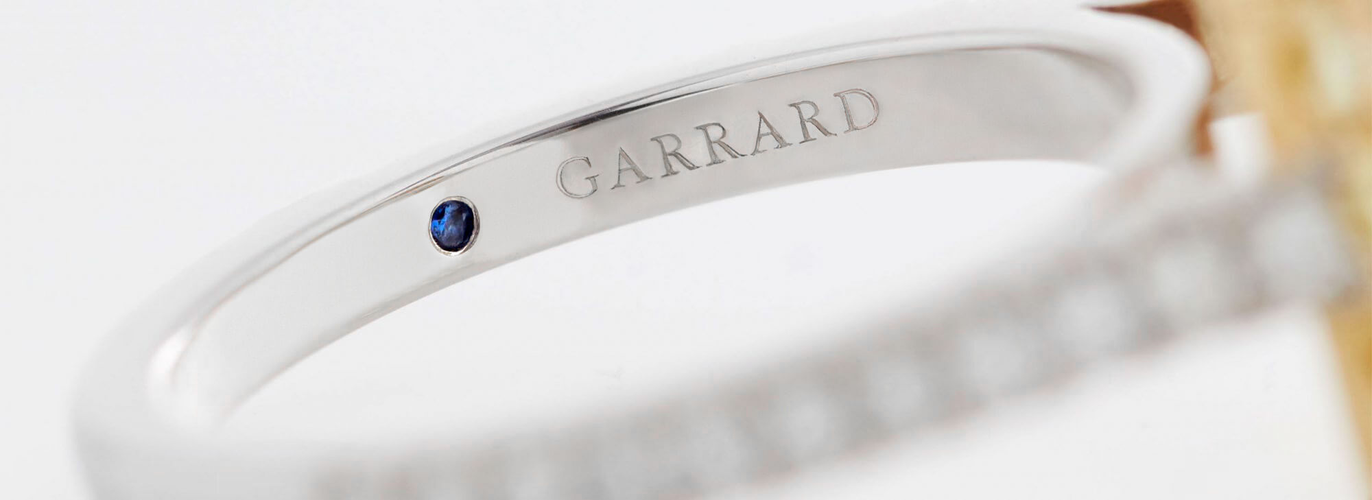 Close up of a Garrard engagement ring with a sapphire indide the diamond band scaled 2000x729 edit