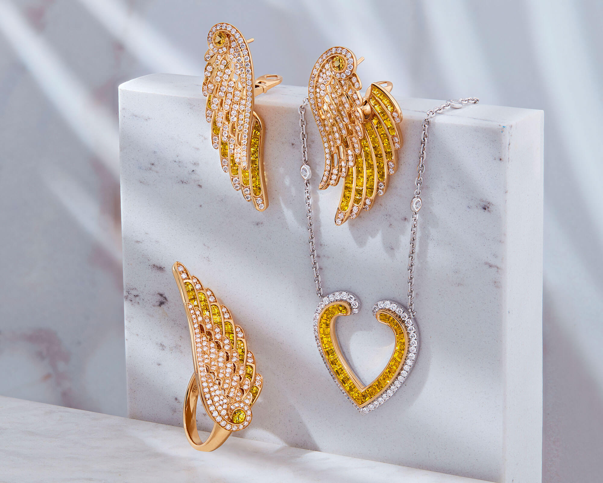 Close up of Wings and Aloria Jewellery collection yellow sapphire and diamond earrings pendant and ring from Garrard marble