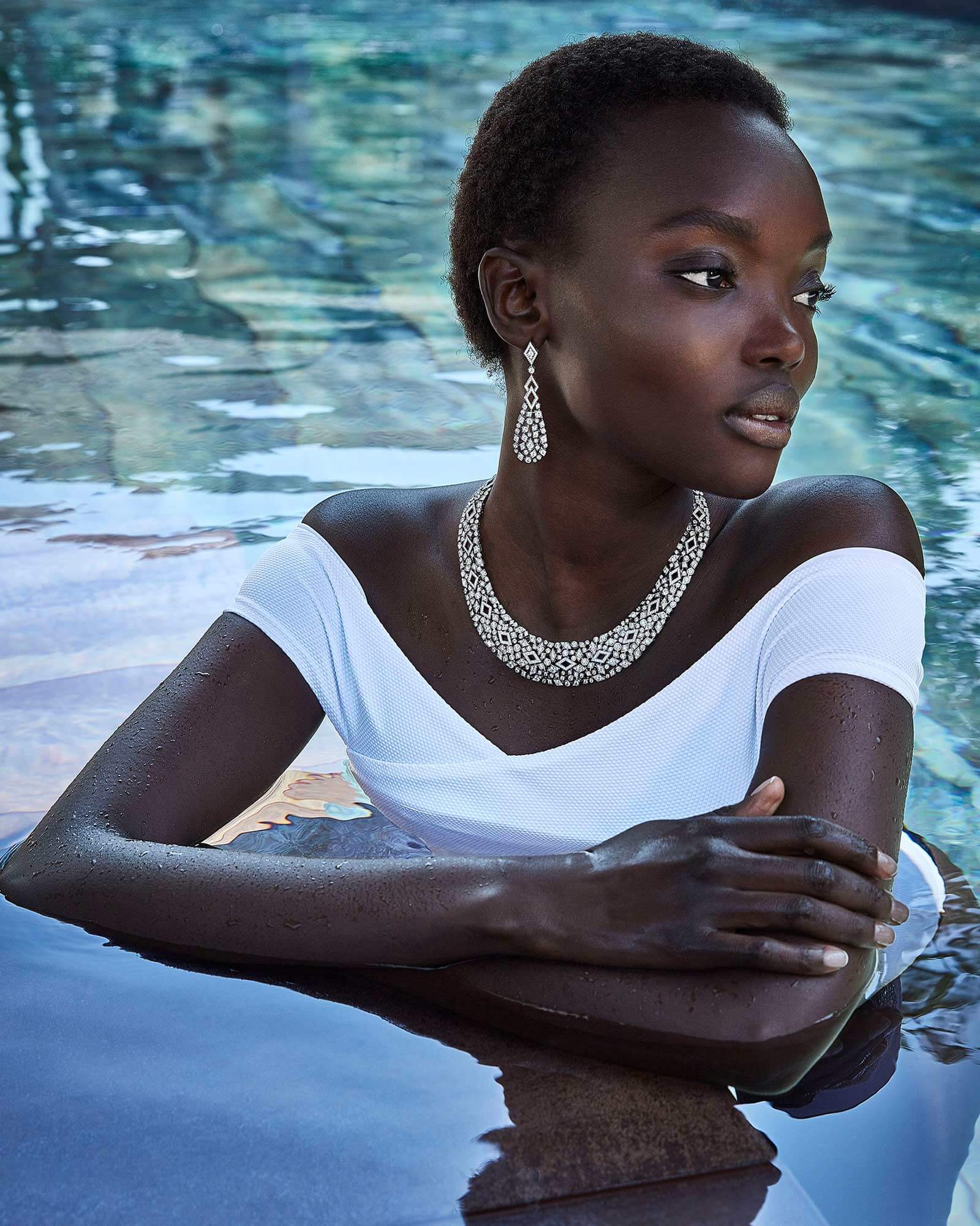 Model wears Garrard Albemarle high jewellery collection diamond earrings and necklace in a pool 4x5